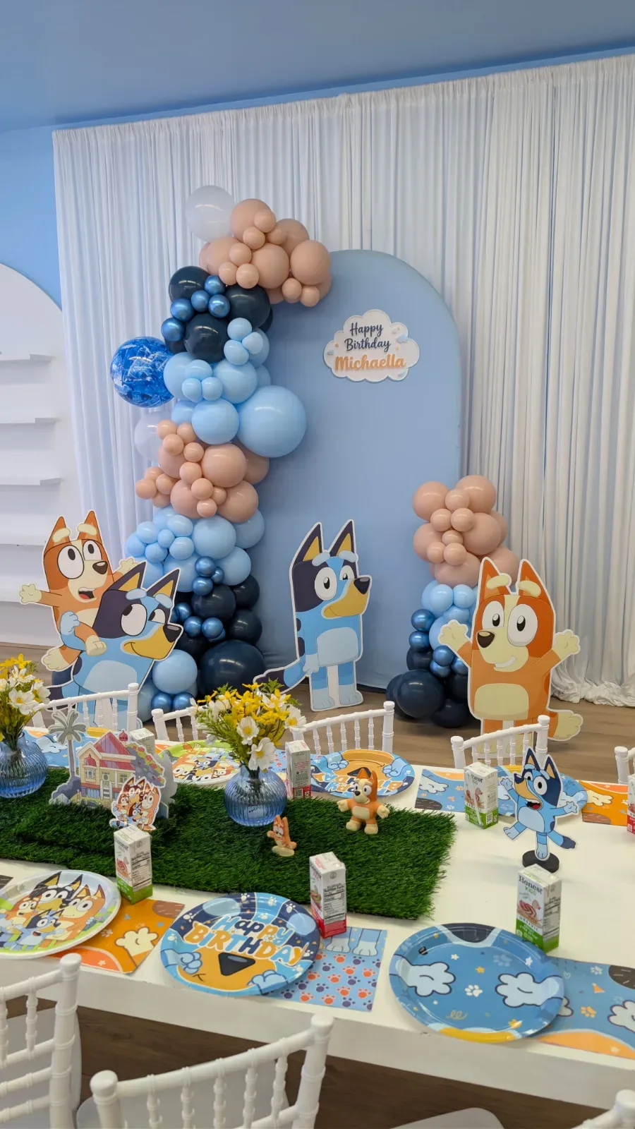 Table decorated in a Bluey theme, featuring a backdrop with a balloon garland and printed Bluey characters.