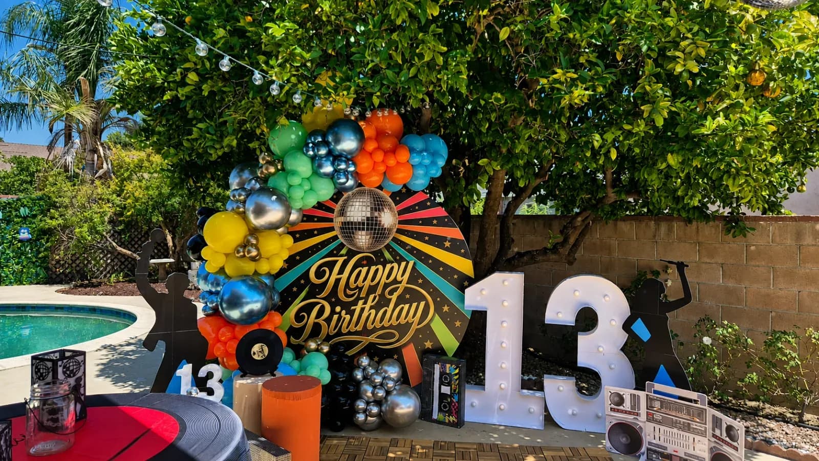 Colorful retro disco 13th birthday balloon backdrop with marquee numbers, disco ball, vinyl records and 1980s party decorations in Los Angeles.