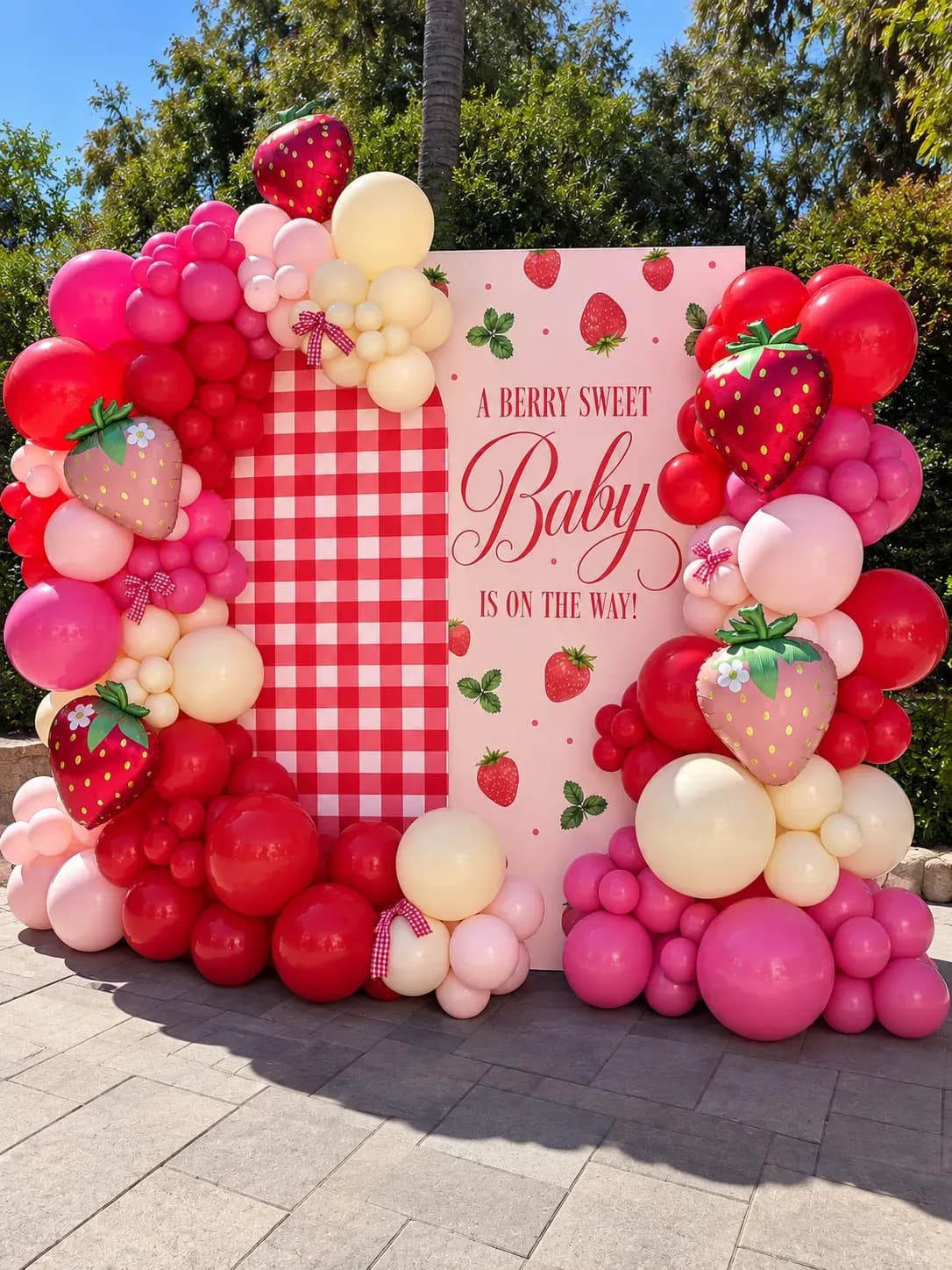 Strawberry baby shower balloon decor in Los Angeles with custom printed backdrop, organic pink red and cream balloon garland, strawberry foil balloons and bow accents